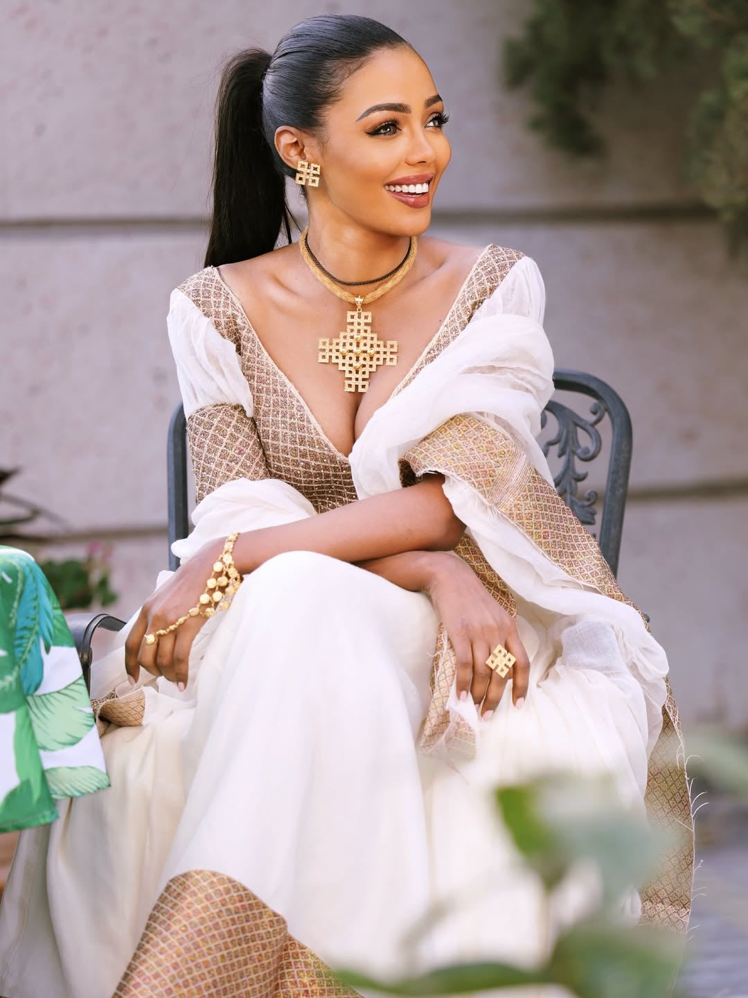 Woman in a white and gold traditional Ethiopian cultural dress sitting outdoors.