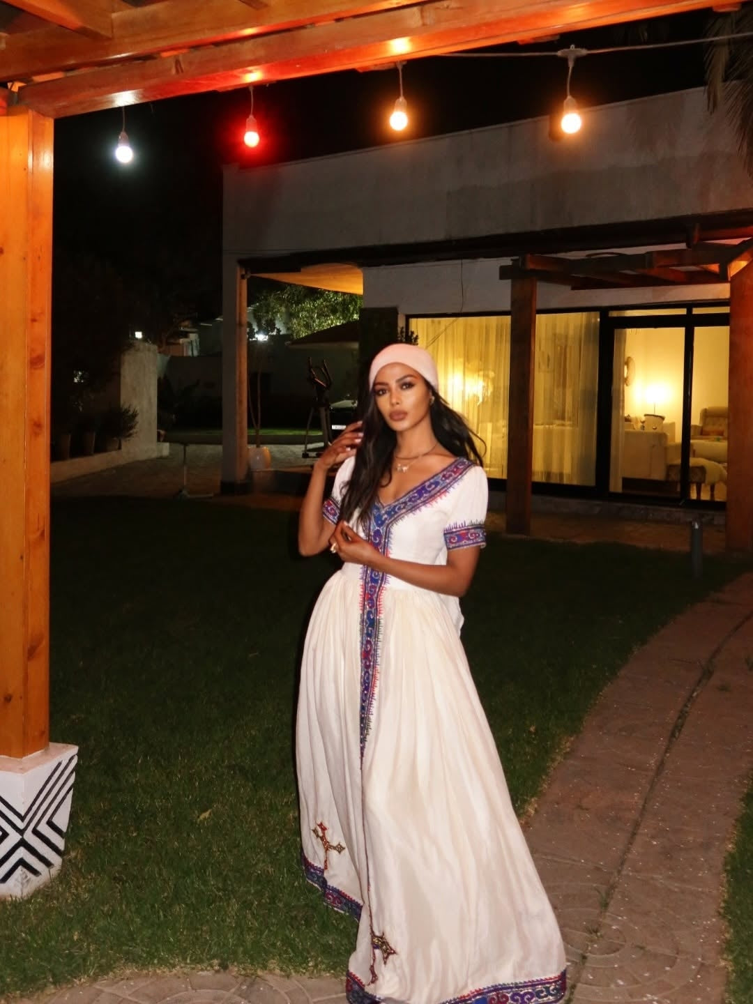 Woman in a habesha dress with blue accents standing outdoors at night.