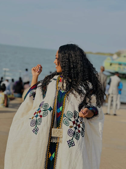 Woman in a Gondar Fetel with intricate patterns standing on a beach.