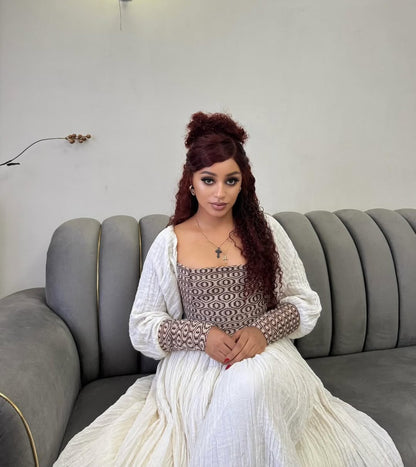 Woman sitting on a gray couch wearing a white and patterned Ethiopian dress.