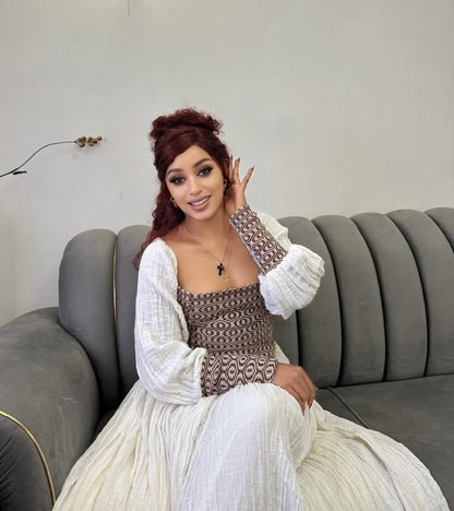 Woman in a patterned Ethiopian dress and white cardigan sitting on a gray couch.