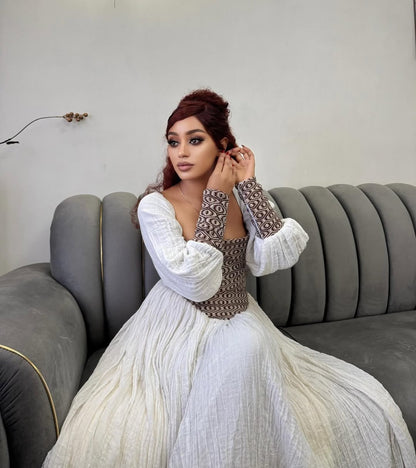 Woman in a white and patterned Ethiopian dress sitting on a gray couch.