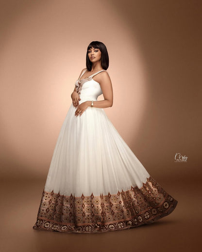 Woman in a white and brown Habesha Kemis  with intricate patterns on a brown background