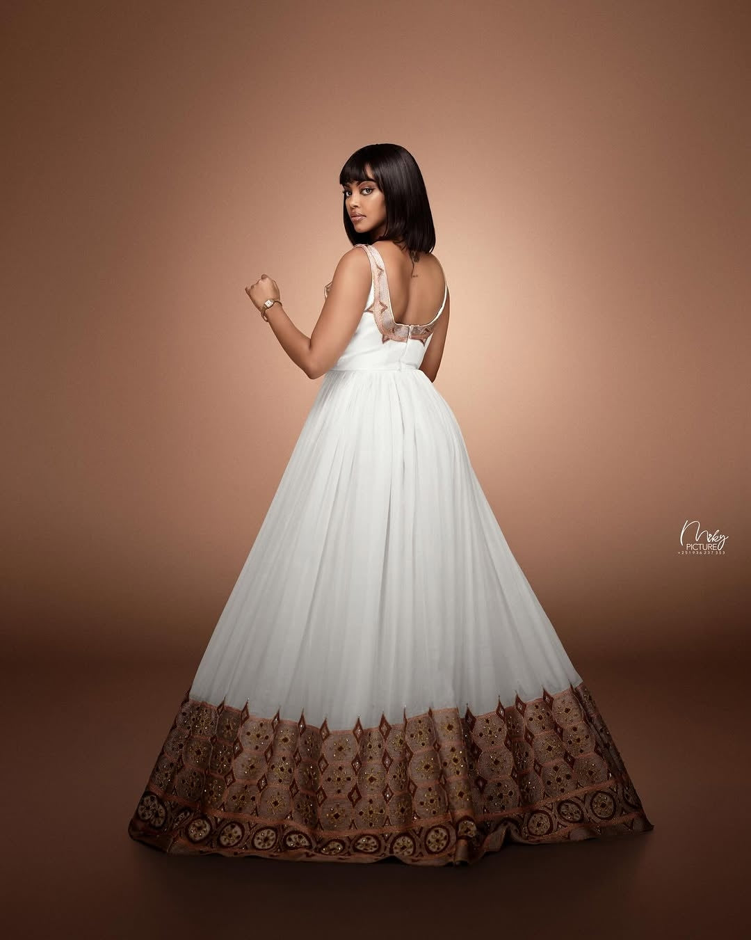 Woman wearing a white gown with brown lace hem on a brown background