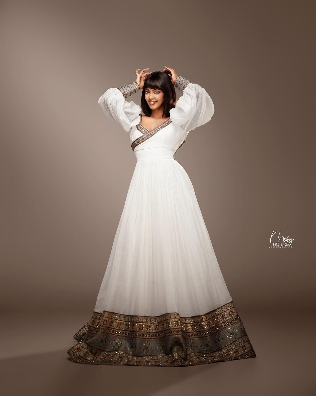 Woman wearing a white dress with patterned hem against a brown background