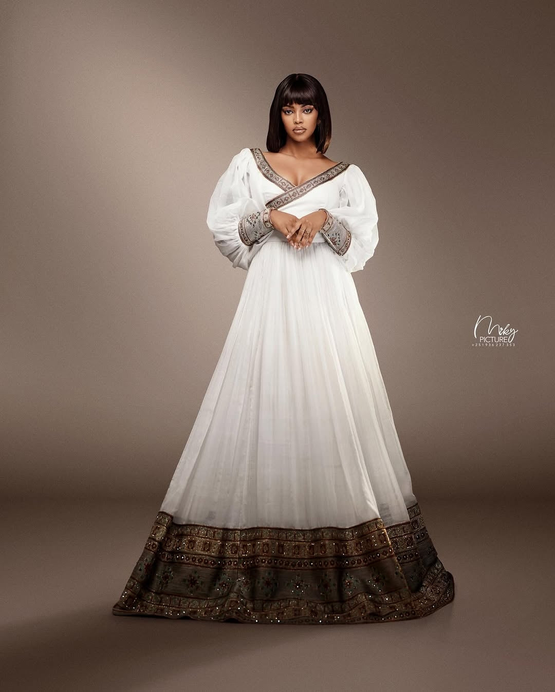 Woman wearing a white dress with brown accents against a brown background