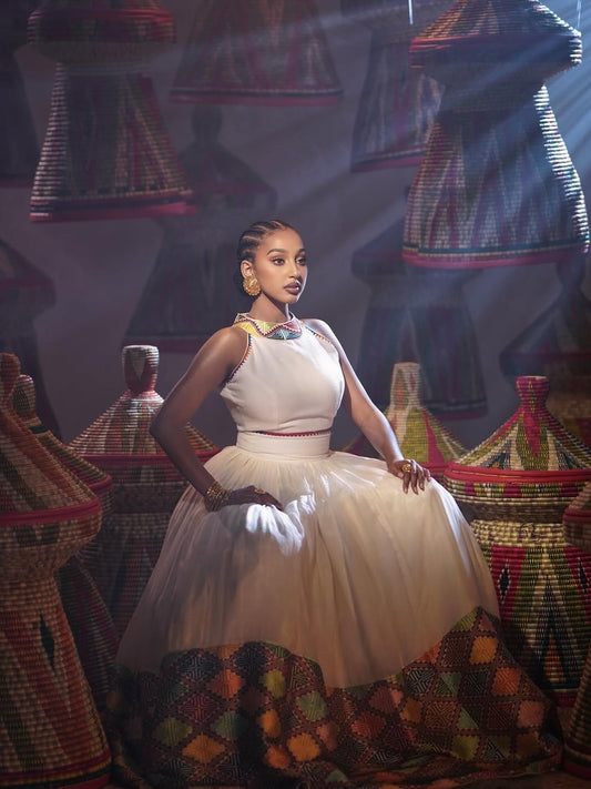 Woman in a white dress standing in front of colorful traditional African garments.