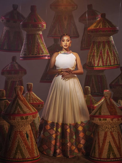 Woman in a white dress standing among traditional woven baskets with geometric patterns.
