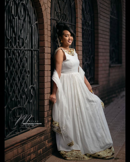Woman in a white Habesha Zuria  standing against a brick wall.