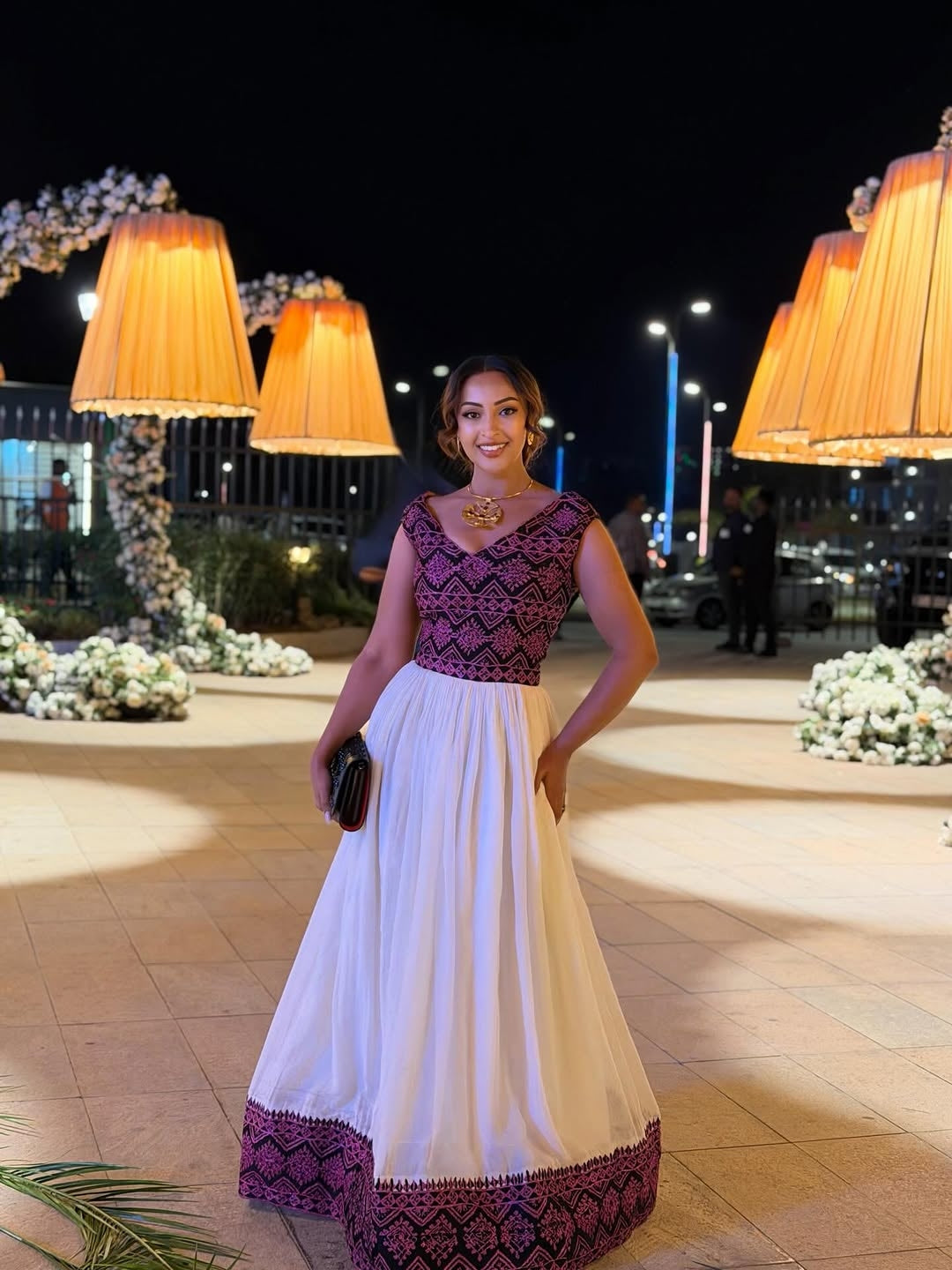 Woman in a  Ethiopian Traditional Dress standing outdoors at night with decorative lights and flowers.