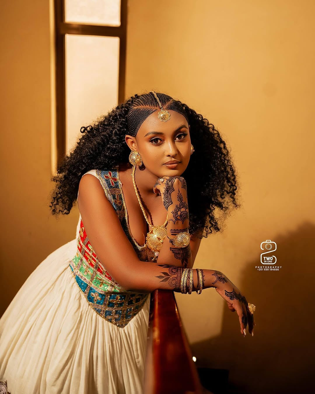 Woman in Ethiopian traditional wedding dress standing on a staircase with a decorative wall in the background