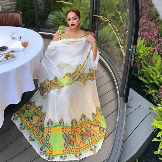 Woman holding a traditional Habesha Dress  with intricate patterns in an outdoor setting.