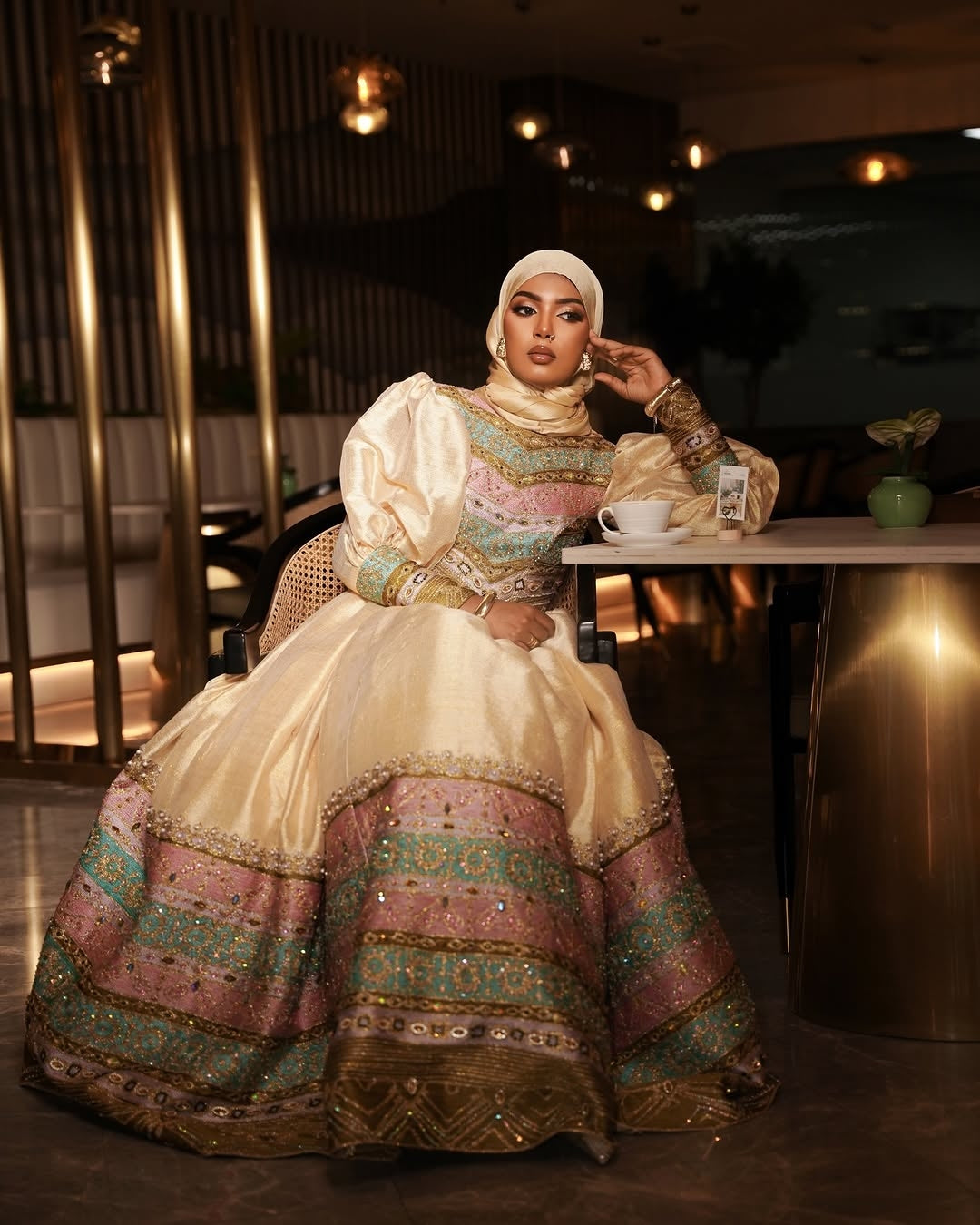 Woman in an ornate habesha dress sitting at a table in a restaurant.