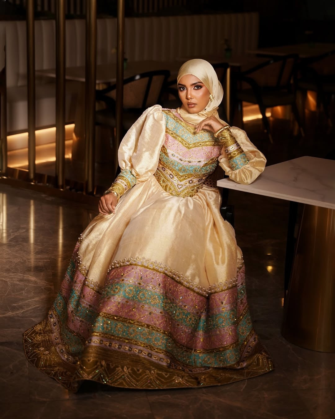Woman in a traditional, ornate habesha dress sitting in a dimly lit room.