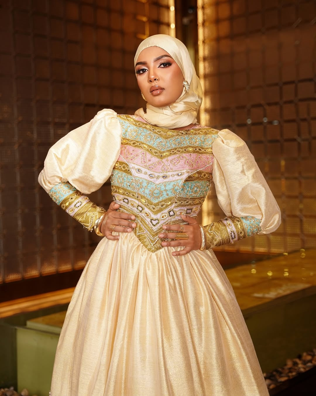 Woman wearing a traditional embroidered dress with a hijab in an indoor setting.
