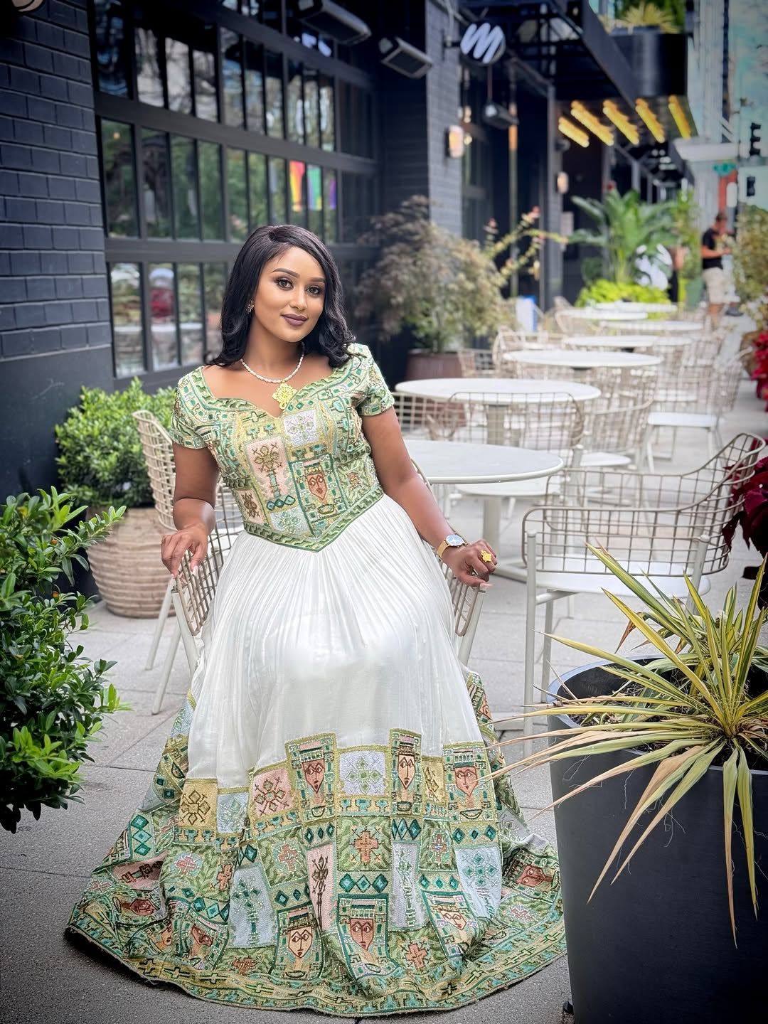 Woman in a traditional habesha kemis standing outdoors with tables and chairs in the background