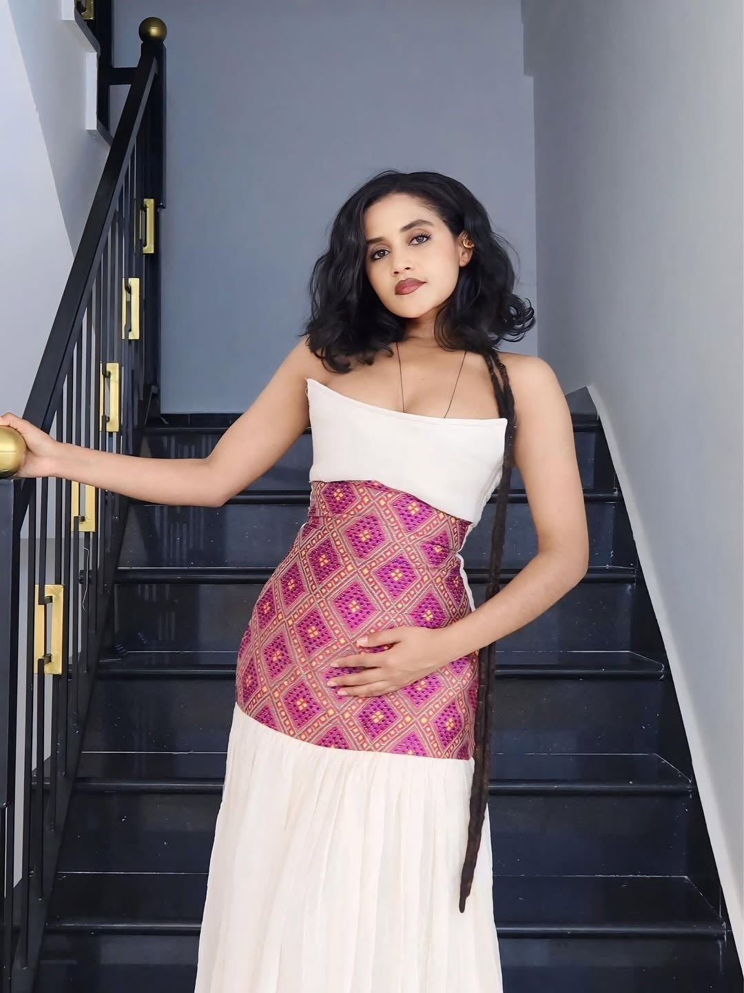 Woman in a white and patterned dress standing on a staircase.