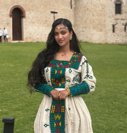 Woman in Ethiopian Traditional Dress embroidered dress standing in front of a stone building
