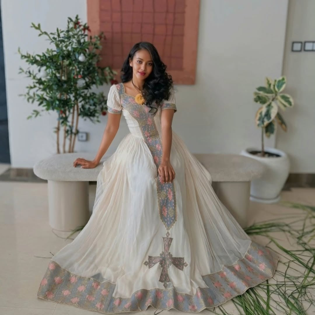Woman in a Ethiopian cultural dress  standing in a modern indoor setting with plants.