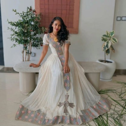 Woman in a Ethiopian cultural dress  standing in a modern indoor setting with plants.