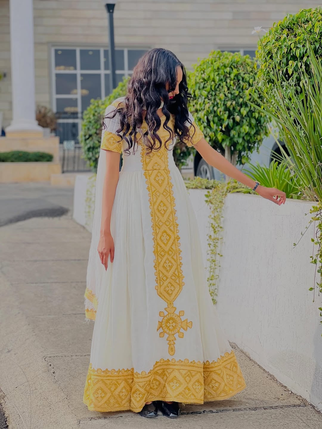 Woman in a white and yellow Habesha kemis with intricate patterns walking outdoors.