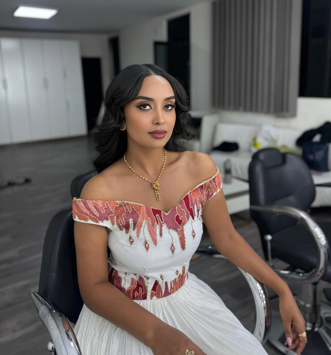 Woman in a white and red Ethiopian cultural dress sitting in a salon chair.