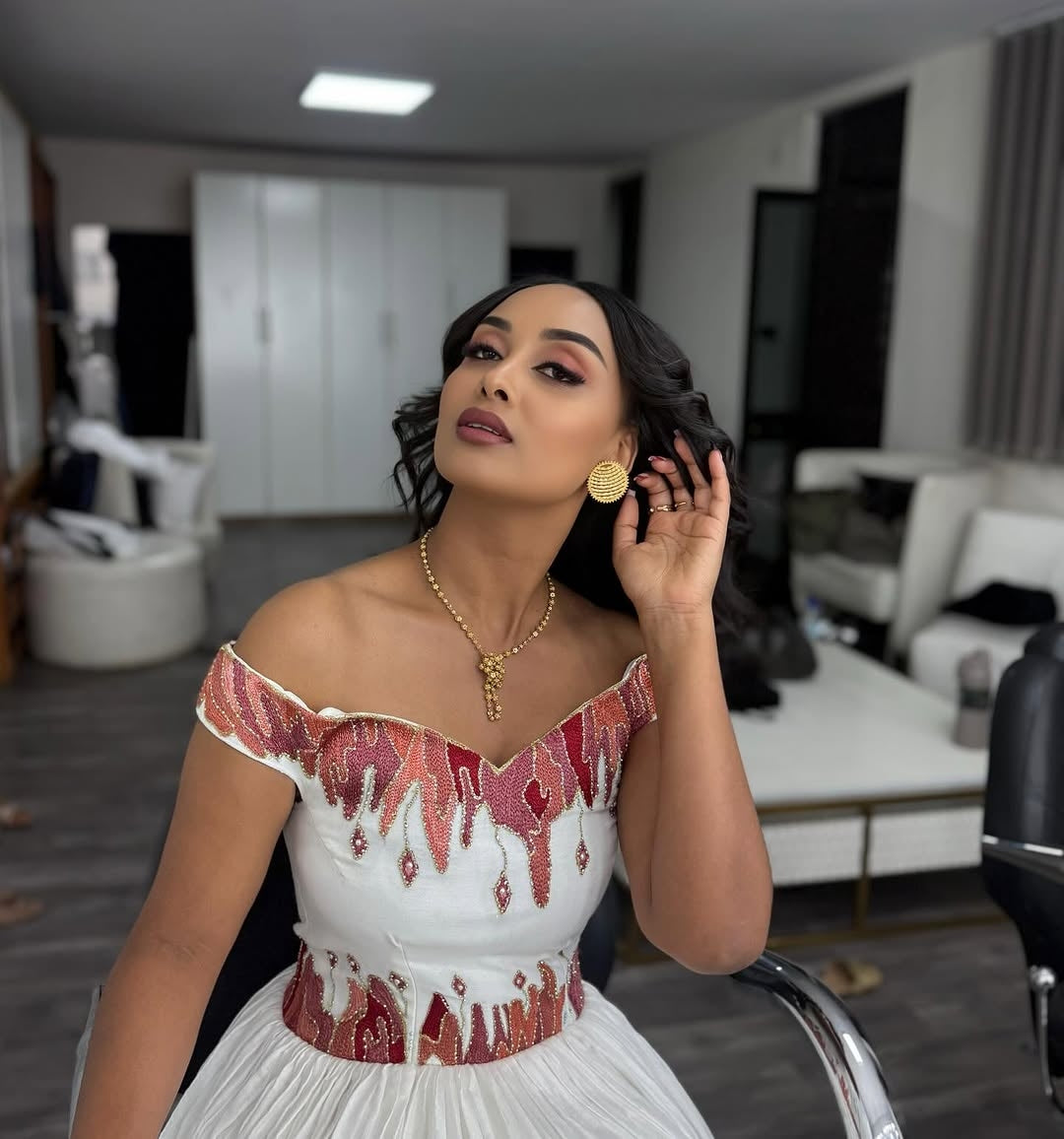 Woman in a white Ethiopian cultural dress with red embellishments in an indoor setting