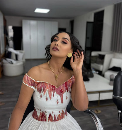 Woman in a white Ethiopian cultural dress with red embellishments in an indoor setting