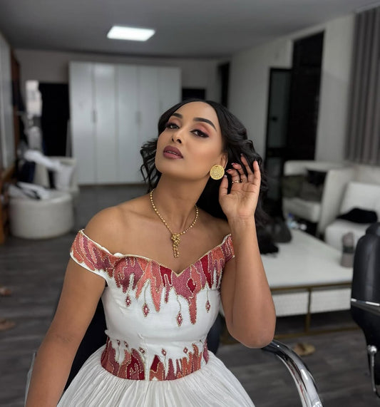 Woman in a white Ethiopian cultural dress with red embellishments in an indoor setting