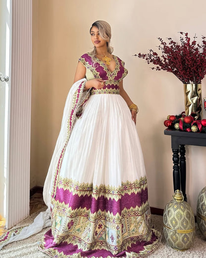 Woman in a traditional Habasha dress   with white and purple patterns, standing indoors.