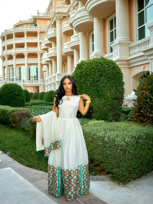 Woman in a white and patterned Ethiopian cultural dress  standing in front of a luxurious building.