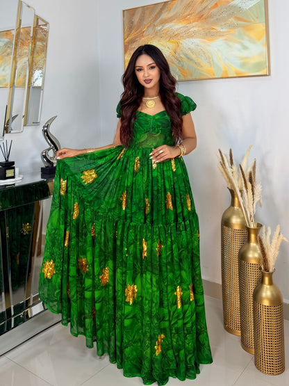 A woman models a vibrant green tiered Habesha Chiffon with gold floral embroidery, standing in an indoor setting with decorative gold vases and a mirror.