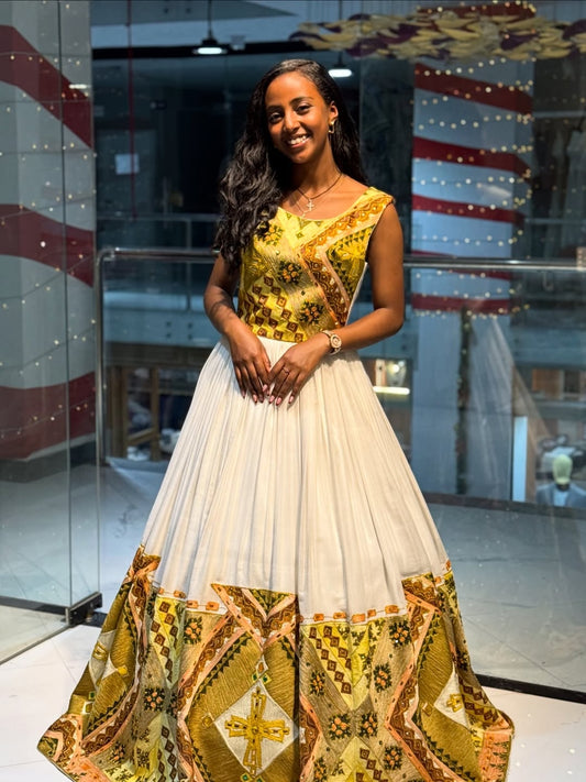 Woman wearing a colorful traditional Habesha Kemis with Gold Tilf Embroidery  with a white skirt in an indoor setting.