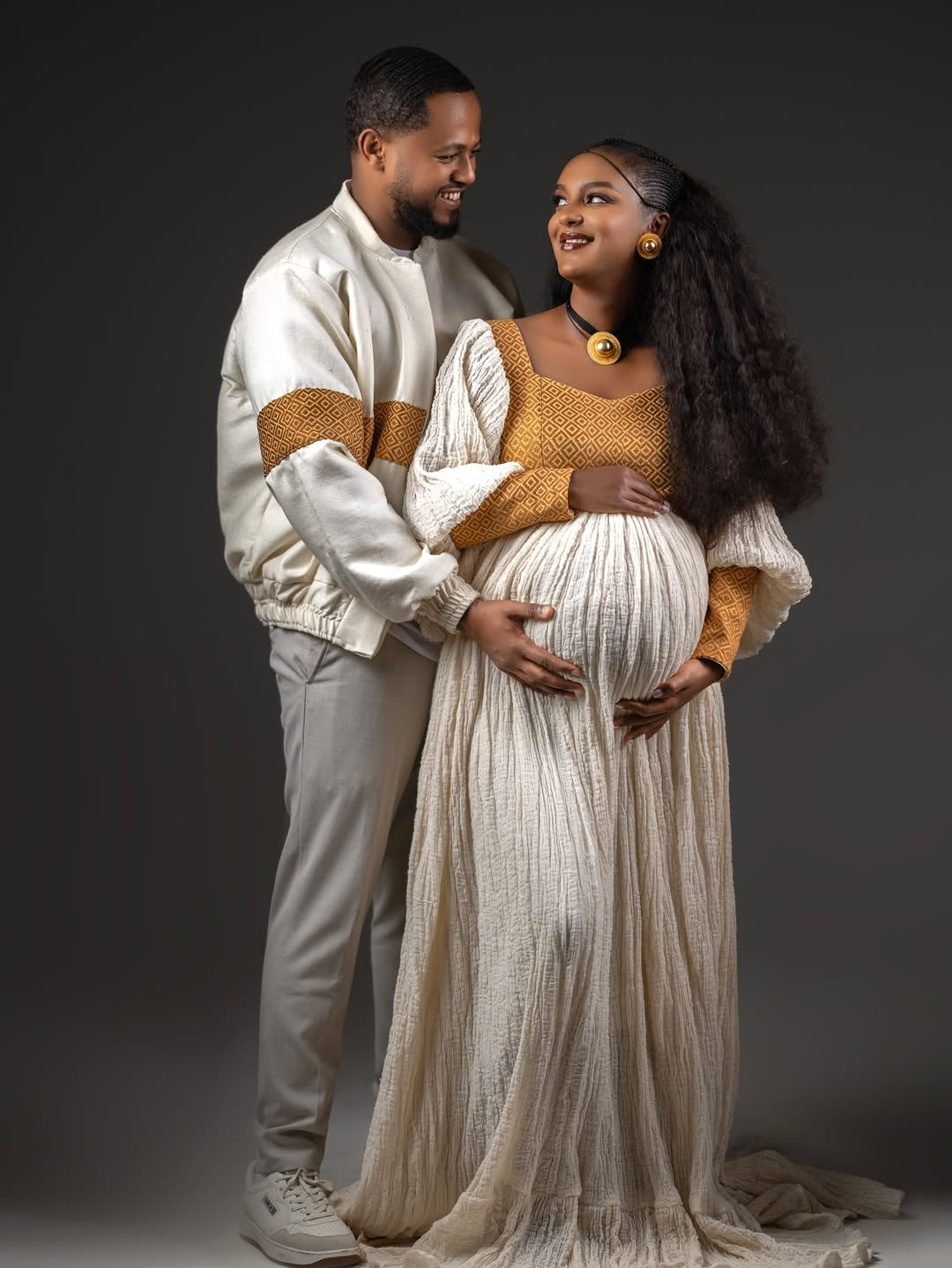 Pregnant woman in a flowing Ethiopian Matching Couple Set with a man in a white outfit against a dark background