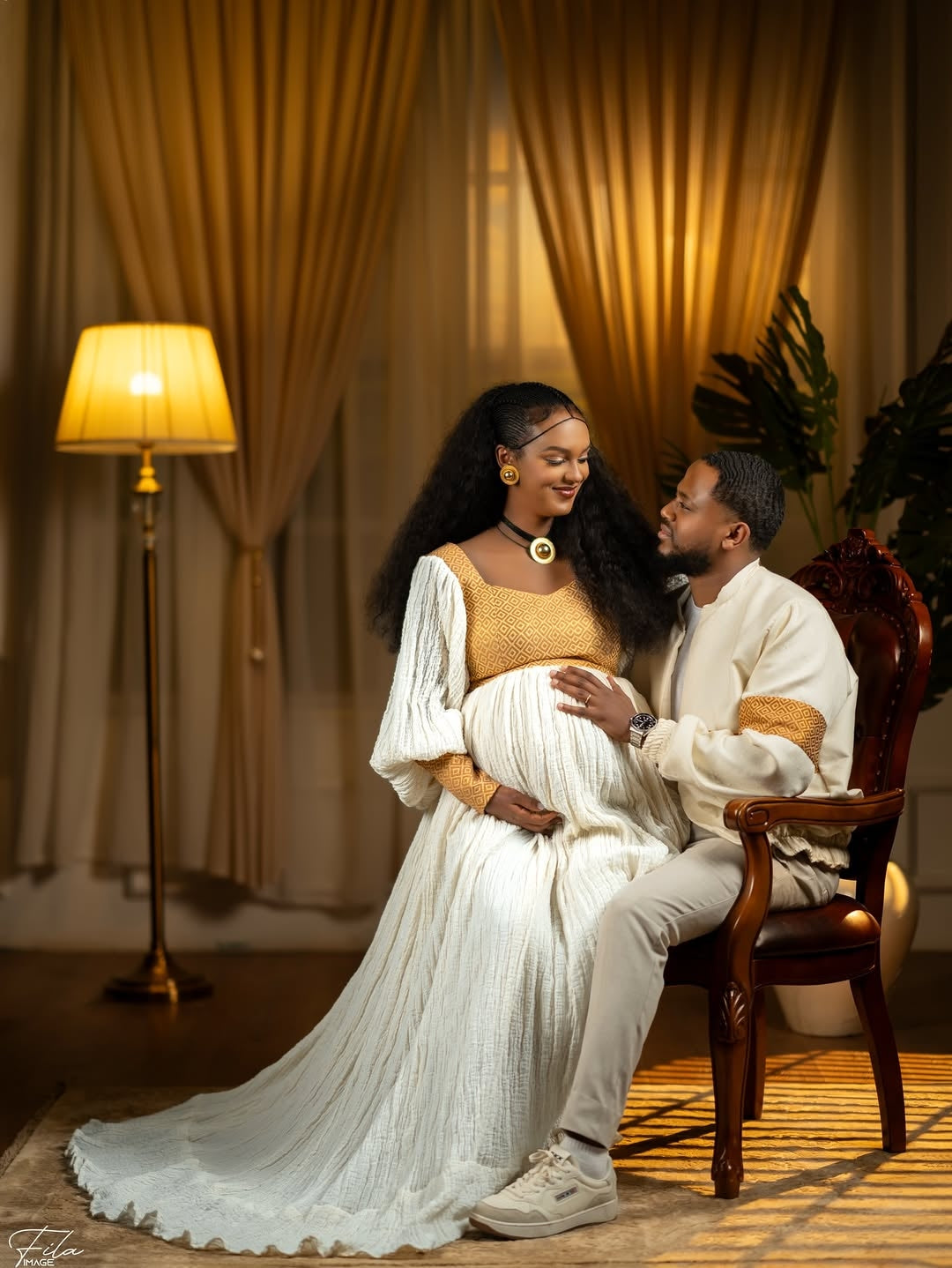 Couple posing together in a warm, indoor Ethiopian Matching Couple Set with draped curtains and a lamp.