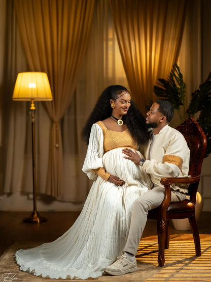 Couple posing together in a warm, indoor Ethiopian Matching Couple Set with draped curtains and a lamp.