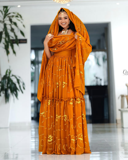 A woman wearing a bright orange traditional Habesha Chiffon  with gold embroidery and a matching draped headscarf, standing in a bright indoor showroom.