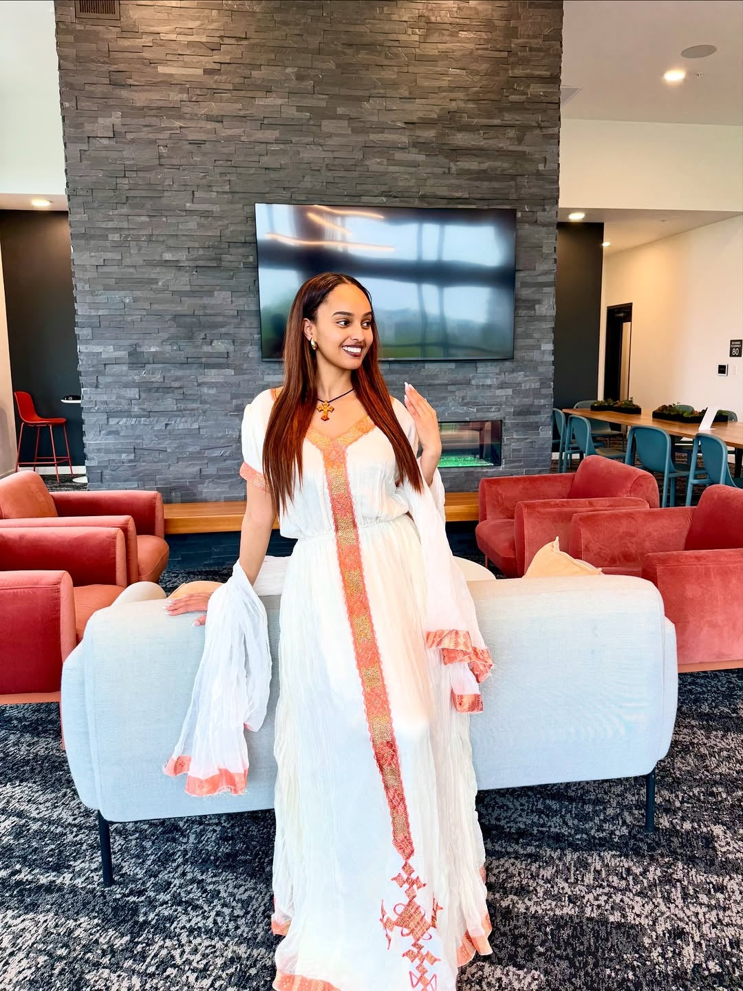Woman in a white and gold habesha dress sitting on a decorative chair in an elegant interior setting.