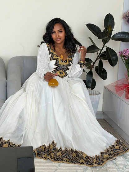 Woman in a white and black Ethiopian Libssitting on a couch with decorative elements.