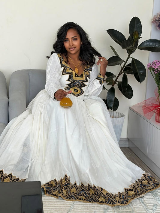Woman in a white and black Ethiopian Libssitting on a couch with decorative elements.