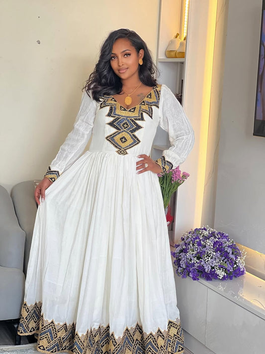 Woman wearing a white Ethiopian Libs and gold patterns in a modern living room.