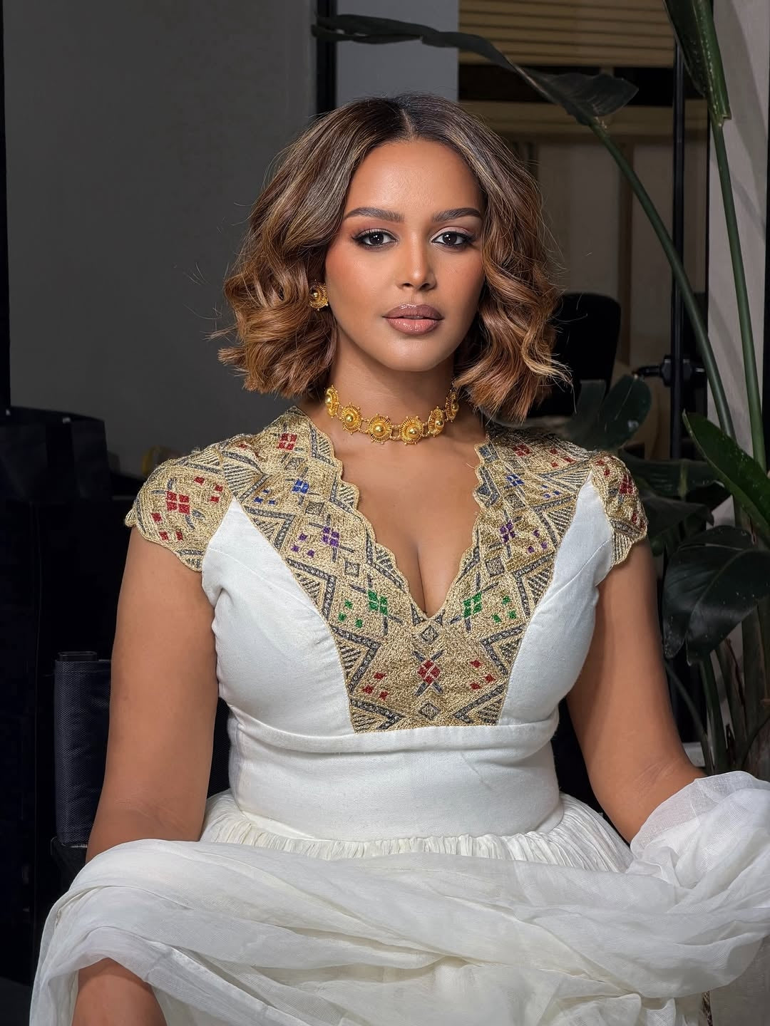 Woman wearing a white Ethiopian Kemis  with a patterned top in an indoor setting