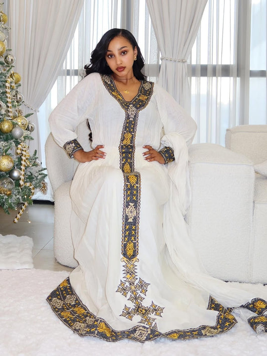 Woman in a white embroidered Ethiopian traditional dress sitting on a couch in a decorated room.