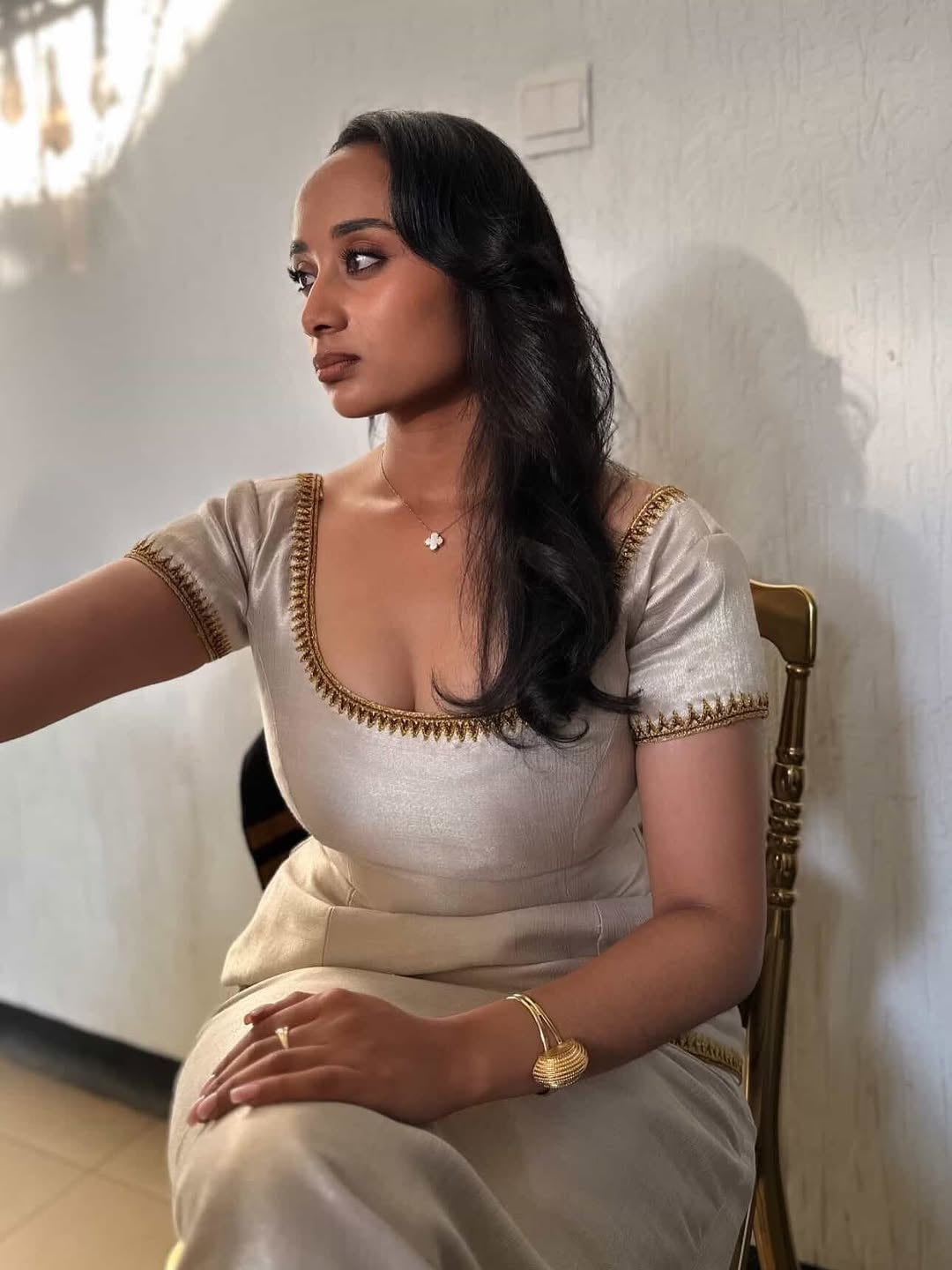Woman in a white traditional Ethiopian cultural dress  with gold accents sitting against a white wall.