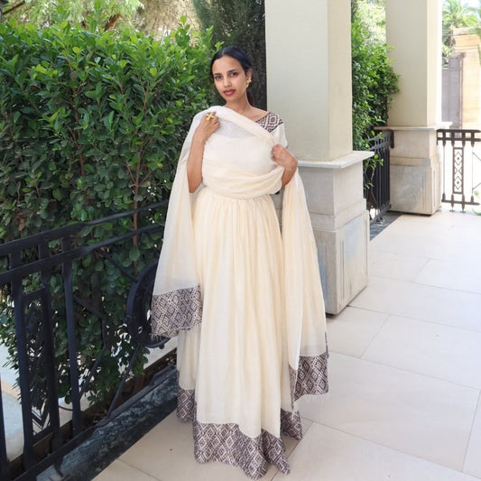 Woman in a white traditional outfit with black patterns standing outdoors.