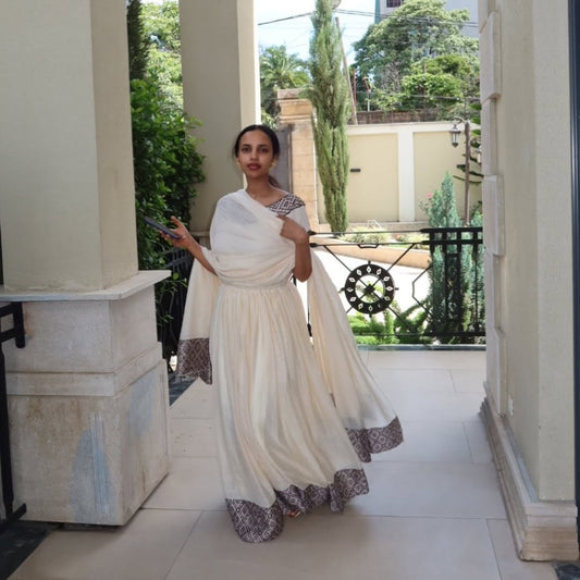 Woman in a white saree with a patterned border standing on a balcony.