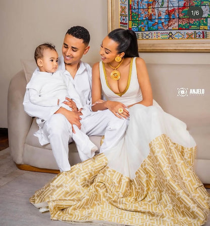 Family of three sitting together on a couch, with a woman in a white and gold dress and a man holding a child.