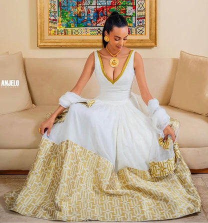 Woman in a white and gold habesha dress sitting on a decorative chair in an elegant interior setting.