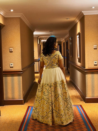 Woman in a yellow and white patterned  Ethiopian traditional dress walking down a hotel hallway.