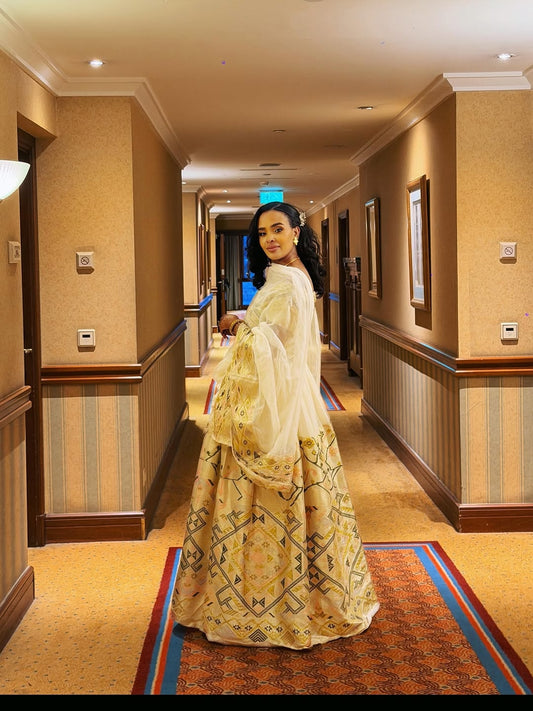Woman in a  Ethiopian traditional dress outfit standing in a hallway with beige walls and carpet.